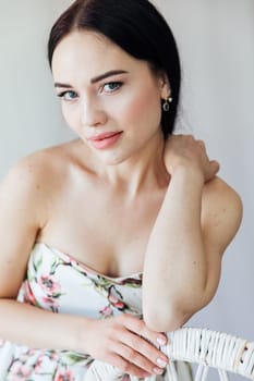 portrait of beautiful brunette woman in a dress by a wicker chair