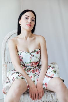 beautiful woman in a floral dress sits in a chair in a bright room