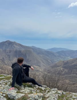 A man sits on mountain and looks into the distance nature hiking on foot travel