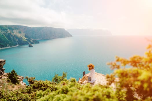 Freelance woman working on a laptop by the sea, typing away on the keyboard while enjoying the beautiful view, highlighting the idea of remote work