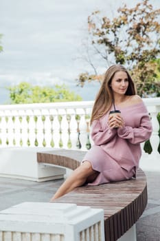 blonde woman sitting on bench with a cup of drink in the park