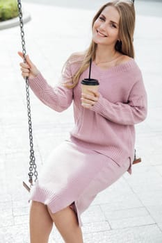 a fashionable woman with a cup rides on a swing