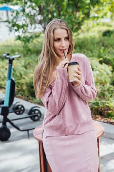 blonde in pink clothes drinks a drink outside on a walk