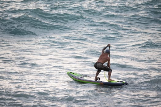 athletic wiry surfer guy swims with a paddle on sup board in the sea Stand up paddleboarding