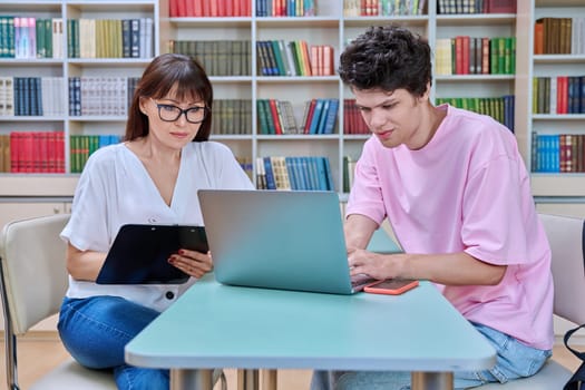 Mature female college counselor, social worker talking with student young male, meeting in library office. Youth mental health, psychology, psychotherapy, help, consultation, mentorship concept