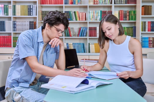 Young male and female students sitting at desk in college library, with books, notebooks, studying, preparing for exams. Knowledge, education, youth, college university concept