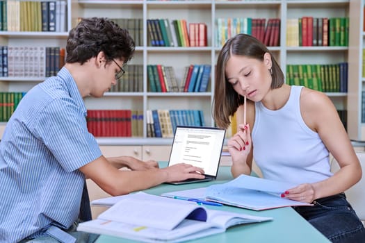 Young male and female students sitting at desk in college library, with books, notebooks, studying, preparing for exams. Knowledge, education, youth, college university concept