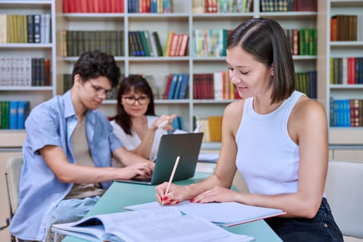 Portrait of student girl at desk inside college library, male student together with teacher preparing for exam. Knowledge, education, youth, college university concept