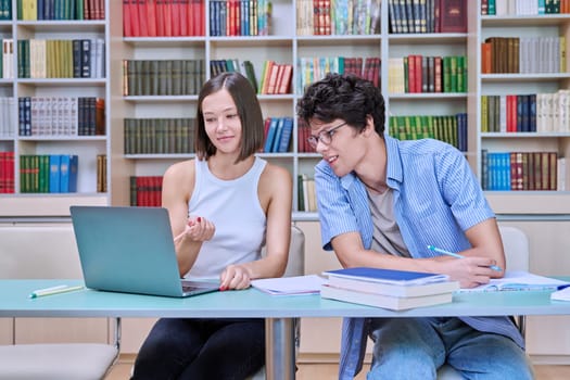 Young male and female students sitting at desk in college library, with books, notebooks, studying, preparing for exams. Knowledge, education, youth, college university concept