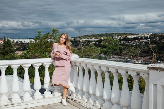 blonde woman stands with a cup of drink at the white railing