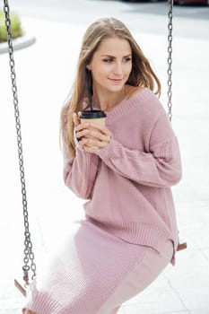 fashionable woman with cup rides on a swing