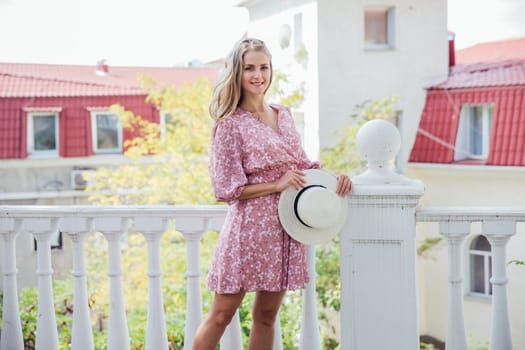 beautiful cheerful blonde in pink dress and hat in her hands walk on the street in the park