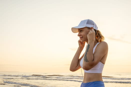 a girl of European appearance in sportswear listens to music on headphones on the seashore during a morning jog. High quality photo
