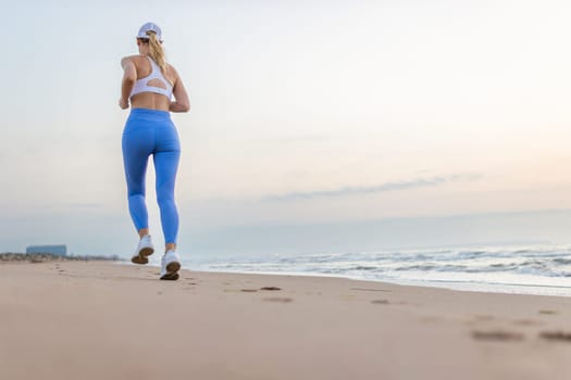 Beautiful sportive woman running along beautiful sandy beach, healthy lifestyle, enjoying active summer vacation near the sea. High quality photo