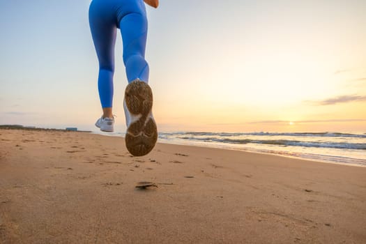 legs of a girl in blue leggings and sneakers running along the beach at dawn with space for inscription. High quality photo