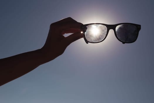 creative photo on the background of blue sky and sunset a girl in her hands holds sunglasses directly above the sun.Summer concept beautiful nature screensaver. High quality photo