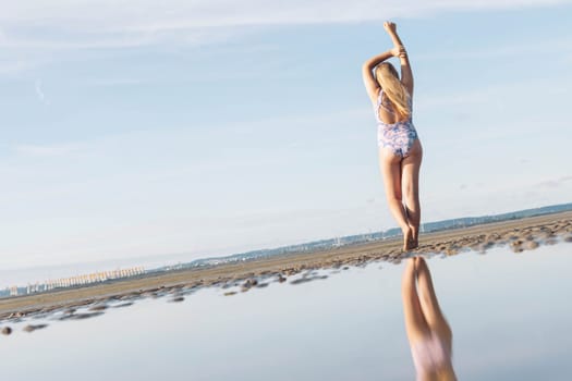 teenage girl in lilac swimsuit stands with her back to her full height on the ocean beach, in front of the photo there is water and on the left there is a place for an inscription. High quality photo