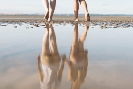 two girls walk on the sand reflection in the water in full growth photo of legs close-up .Beautiful landscape of the beach. High quality photo