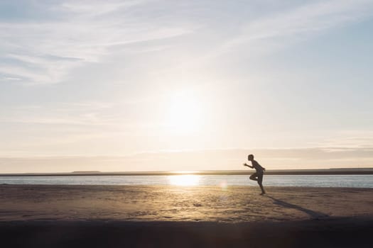 a boy runs on the beach at sunset, a silhouette of a child running on the beach on the sand near the water, there is a place for an inscription. High quality photo