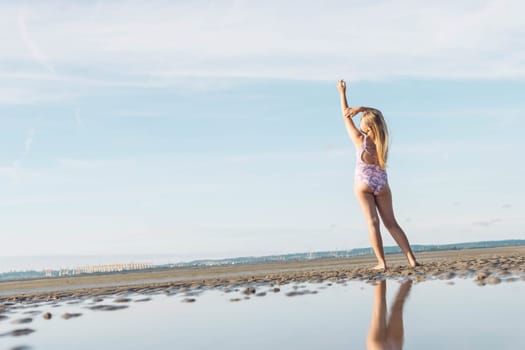 teenage girl in lilac swimsuit stands with her back to her full height on the ocean beach, in front of the photo there is water and on the left there is a place for an inscription. High quality photo