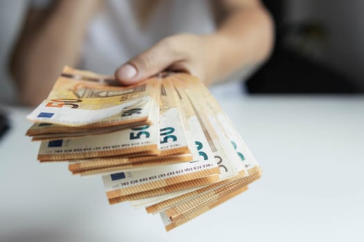 a girl in a white t-shirt stretches her hand forward holding euro 50 banknotes in her hand close-up focus on money background blurred. High quality photo