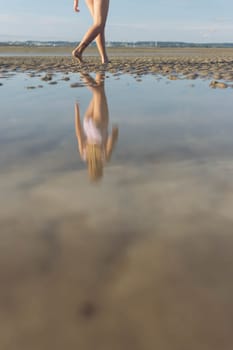 a girl in a bathing suit goes forward to the sea, a reflection in the water in full growth, a photo of women's legs on the beach. High quality photo
