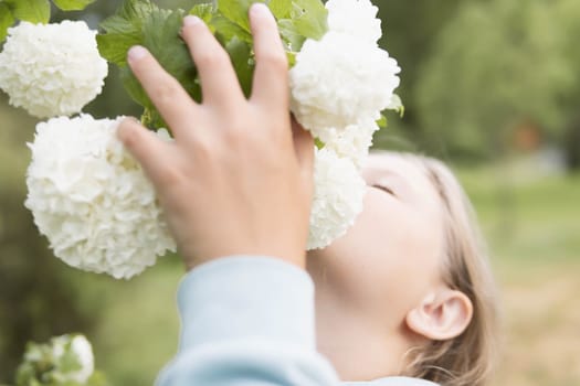 A teenager of European appearance with blond hair stands sniffing white flowers on a tree.Flowers in focus. High quality photo