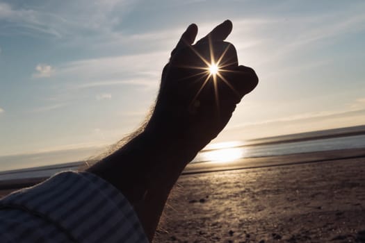 man's hand is isolated against the background of the sky, the ocean and sand on the beach. a hand at sunset. A beautiful landscape, on the right there is a place for an inscription. High quality photo