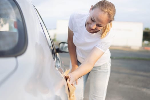 a girl with blond hair in a white T-shirt and jeans, bending over wipes the car after washing with a special yellow rag with microfiber. The concept of cleanliness. High quality photo
