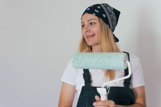a girl with blond hair in a bandana, stands posing at the camera with a roller for painting walls. stands facing the camera cheerful. there is a place for an inscription. High quality photo