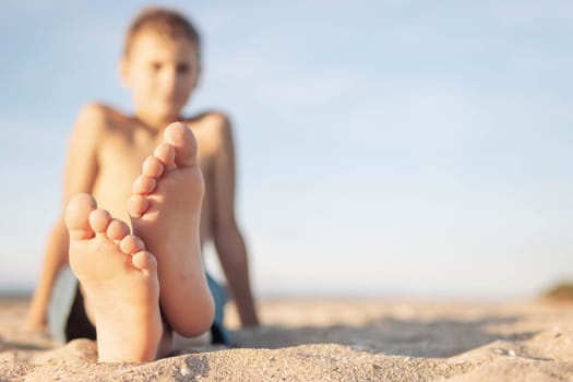 a child of European appearance sits on the sand on the beach close-up of legs and feet in focus the body of a blurry boy on the right there is a place for an inscription. High quality photo