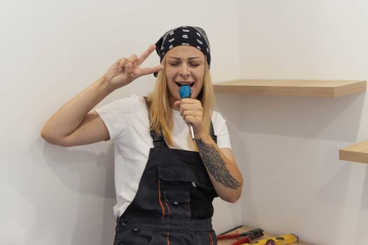 a girl of European appearance in a white T-shirt and work overalls on her head with a black bandana, sings songs in a screwdriver and have fun at work on her left arm tattoo. High quality photo