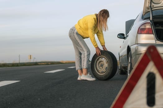 girl stands near the rear wheel of the car and rolls the spare wheel to change, the wheel has been pierced. Close-up there is a place for an inscription High quality photo