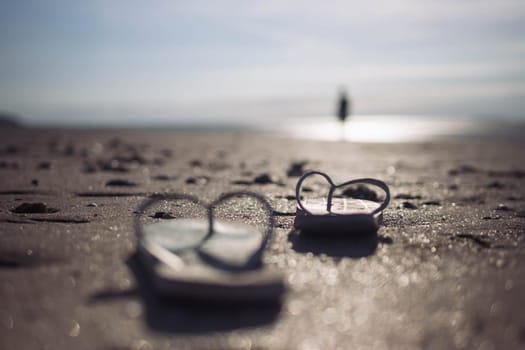 on the beach on the sand, a pair of beach slippers stands close-up and the background is blurred at sunset, the photo is taken, a beautiful and creative beach background High quality photo