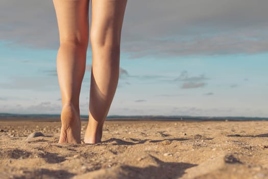 female legs against the background of the sky and sand on the beach. Female legs against the background of a sunset. Beautiful landscape, with a place for an inscription.High quality photo