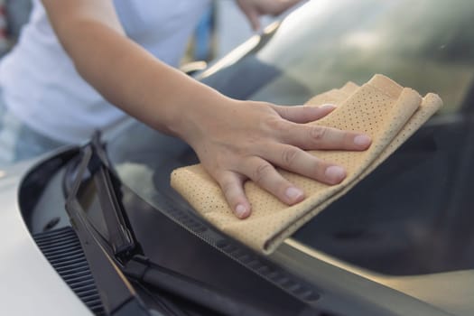 A girl in a white t-shirt wipes the window in the car with a yellow special window cloth.Close-up of a hand and a rag.Work and cleanliness concept. High quality photo