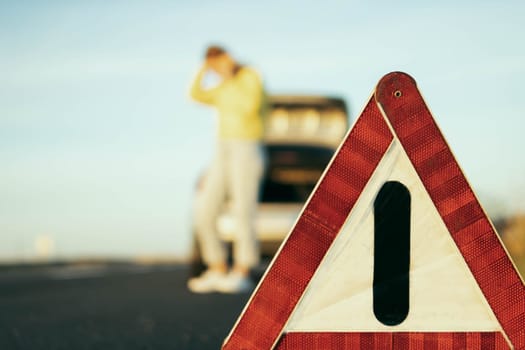 in the foreground is a red-white close-up warning triangle, in the background a girl in a yellow sweater and jeans stands with her hand raised, speaks on the phone,High quality photo