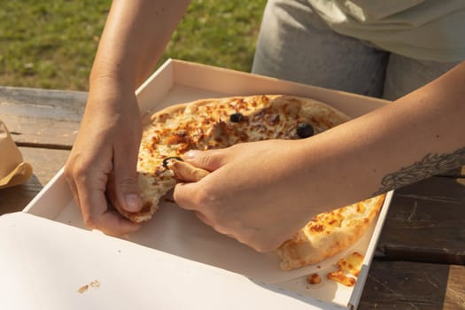 a girl with a tattoo on her arm in the shape of a wing breaks pizza at a picnic in the park, hands and pizza close-up. High quality photo