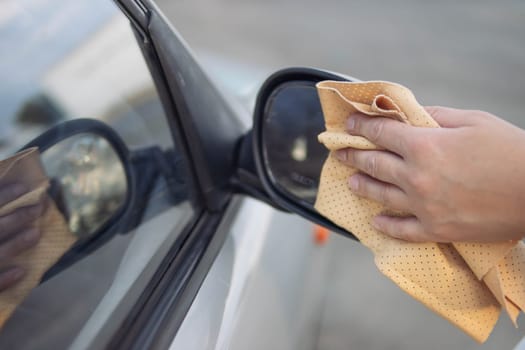 girl wipes the side window in the car with a yellow special cloth for windows.Close-up of a hand and a rag.there is a place for an inscription. The concept of work and cleanliness. High quality photo