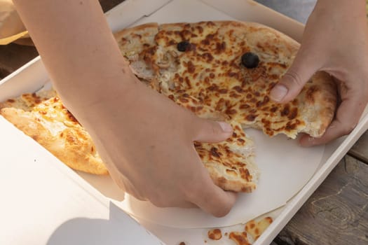 a girl breaks pizza with her hands in the park on a wooden table.outdoor picnic with family pizza is in a white cardboard box. High quality photo