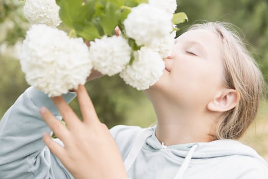 A teenager of European appearance with blond hair stands sniffing white flowers on a tree.Flowers in focus. High quality photo