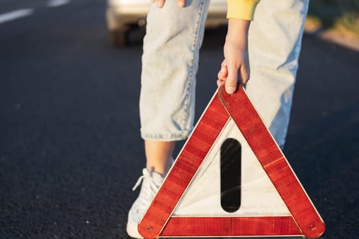 a girl puts an emergency stop sign on the highway near a broken car close-up on the sign. A car breakdown on the highway, there is a place for an inscription. High quality photo