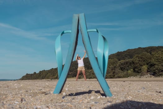 close-up of blue flip-flops standing on the sand between them a small photo of a girl in a white t-shirt and brown shorts standing between slippers with her hands up.Creative photo High quality photo