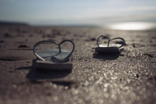 on the beach on the sand, a pair of beach slippers stands close-up and the background is blurred at sunset, the photo is taken, a beautiful and creative beach background High quality photo