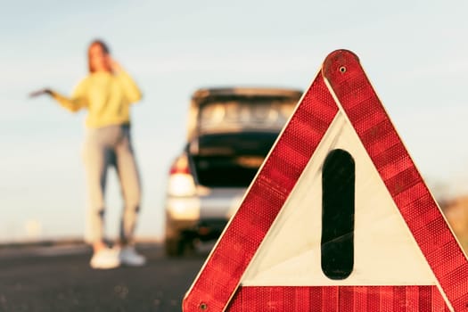 in the foreground is a red-white close-up warning triangle, in the background a girl in a yellow sweater and jeans stands with her hand raised, speaks on the phone,High quality photo