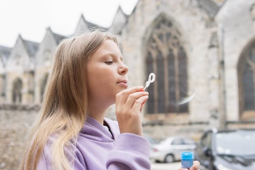 a girl of European appearance with blond hair in a lilac sweater plays with bubbles on the street. High quality photo