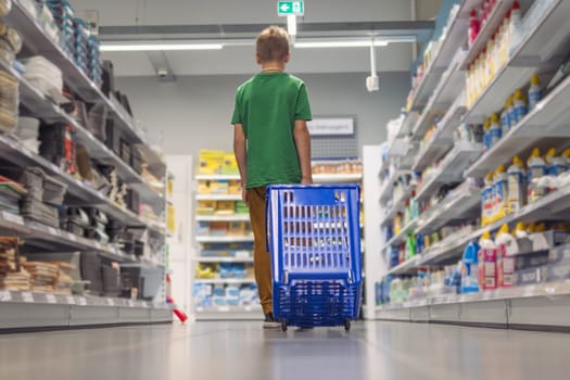 a boy of European appearance with blond short hair in a green T-shirt in a store with his back turned with a blue shopping cart, walks and chooses toys. High quality photo