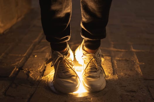 a girl stands in the evening on a lantern on the pavement legs close-up.girl in white sneakers and black pants. High quality photo