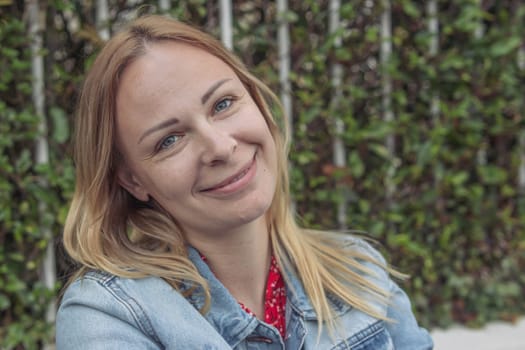 a girl with blond hair in a denim jacket sits in a park dreaming and smiling close-up, portrait .human emotions. High quality photo