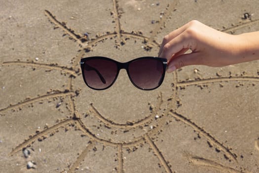 on the beach on the sand the sun is drawn with rays and next to glasses instead of eyes lie a beautiful beach background with a place for an inscription. High quality photo